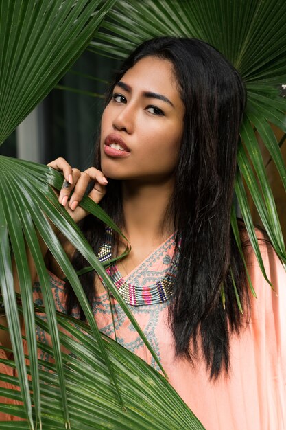 Close up portrait of beautiful thai woman over tropical leaves. Spa and relax concept.Ethnic boho style.