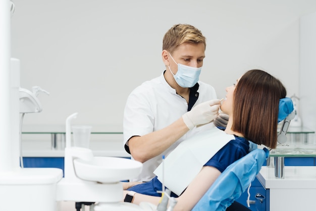 Close up portrait of beautiful young lady sitting in dental chair while stomatologist hands in sterile gloves holding tooth samples