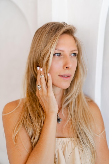 Close up portrait of blond woman in casual outfit posing over stylish beige interior Accsessorises tropical mood vacation time