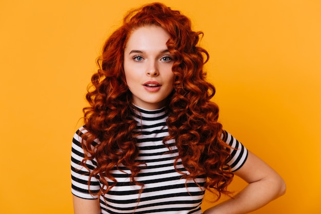 Free photo close-up portrait of blue-eyed girl with long eyelashes and voluminous red curly hair against orange space.