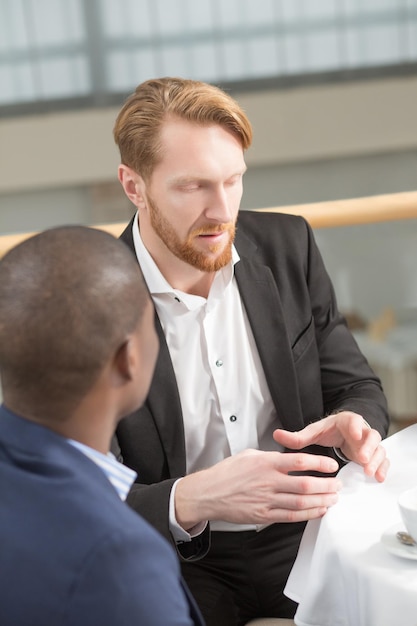 Free photo close-up portrait of businessman explaining something to his foreign business partner while sitting at table during business meeting in restaurant.