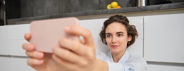 Free photo close up portrait of candid young woman takes selfie on smartphone using mobile phone photo app with