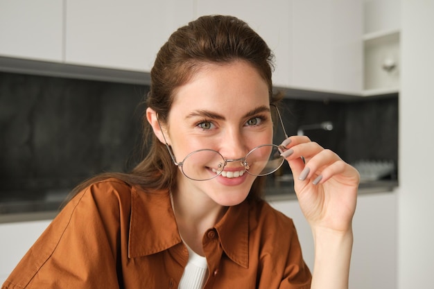 Free photo close up portrait of carefree woman in glasses sitting at home in kitchen smiling and looking happy