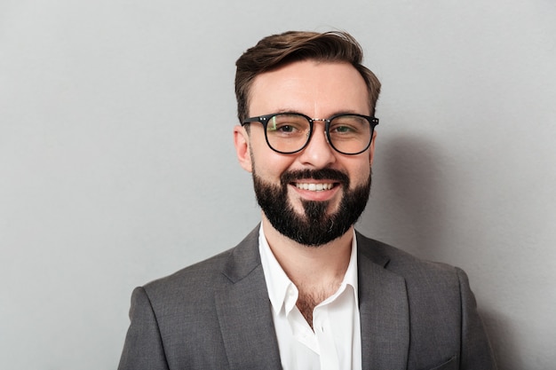 Close up portrait of caucasian unshaved man in eyeglasses looking on camera with sincere smile, isolated over gray