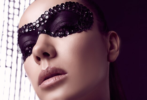 Close-up portrait of charming elegant brunette woman in sequins mask posing on black