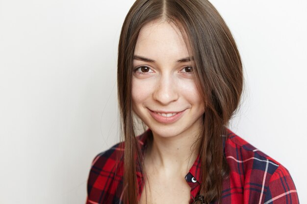 Close up portrait of cheerful young brunette woman with cute smile and healthy clean skin wearing her messy braid on side, smiling happily