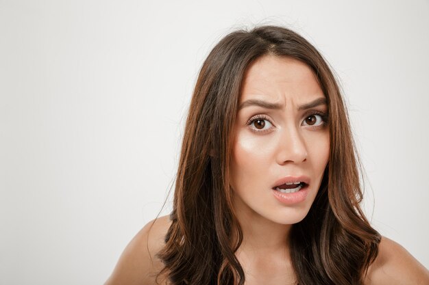 Close up portrait of confused caucasian woman looking on camera in puzzlement with facial expressions, isolated over white