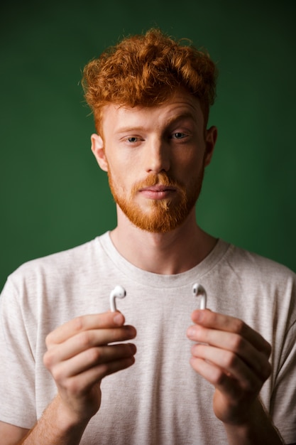 Close-up portrait of curly redhead man with raised eyebrow, showing his airpods,