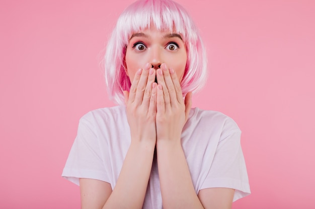 Free Photo close-up portrait of cute shocked young woman posing  in pink peruke. indoor shot of frightened girl in periwig isolated on pastel wall