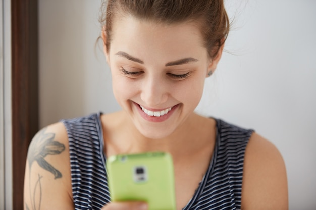 Free photo close-up portrait of dark-haired female with white skin sending messages to her friends in the internet. social communications through our gadgets can be really funny and joyful. positive concept.