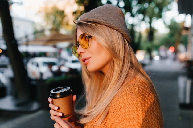 Free photo close-up portrait of dreamy fair-haired woman waiting friend outdoor and drinking latte