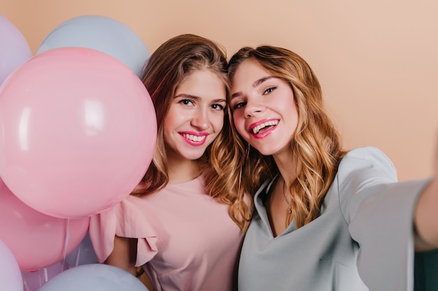 Close-up portrait of excited woman with curly hair making selfie with friend