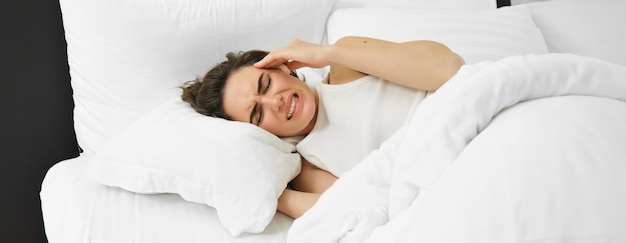 Free photo close up portrait of female model lying in bed with headache grimacing and frowning from painful