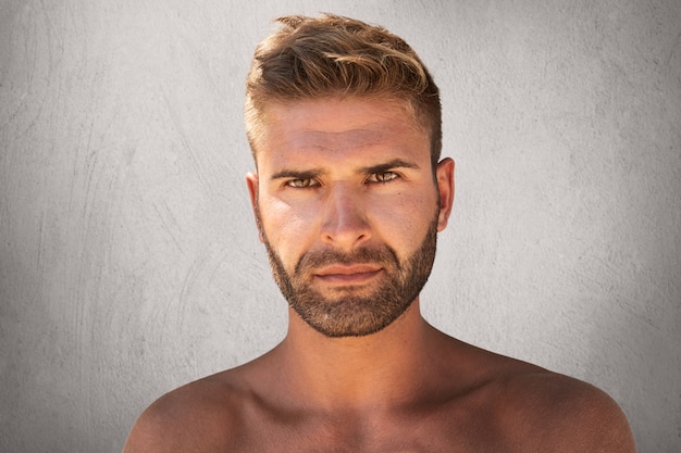 Close up portrait of good-looking male with dark eyes, bristle and trendy hairdo being naked