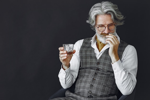 Free photo close up portrait of grinning old-fashioned man.  grandfather with a cigar and whiskey.