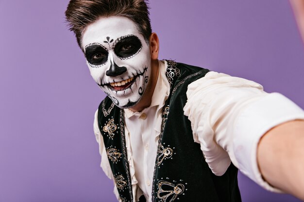 Close-up portrait of guy in great mood. Young man with face art makes selfie.