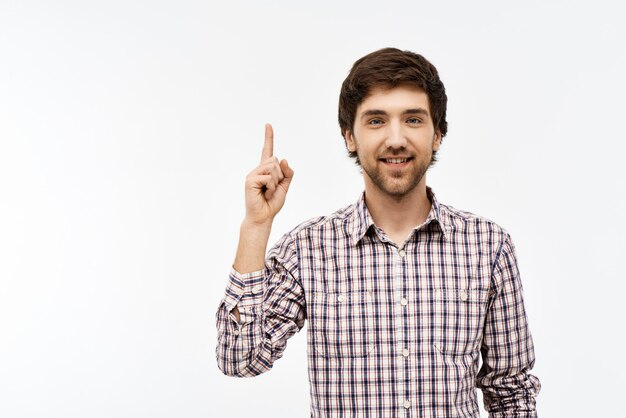 Close-up portrait of handsome confident young blue-eyed dark-haired man wearing casual plaid shirt looking at front, pointing up