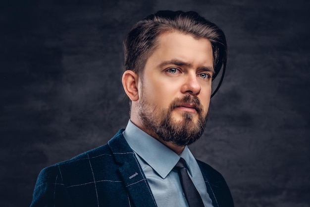 Free photo close-up portrait of a handsome middle-aged man with beard and hairstyle dressed in an elegant formal suit on a textured dark background in studio.