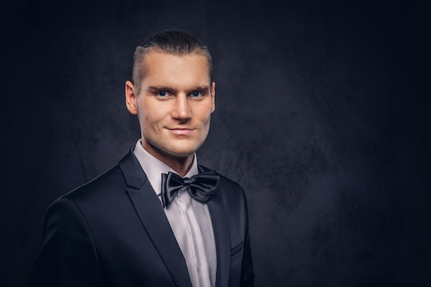 Close-up, a portrait of a handsome stylish man in an elegant black suit over a dark background.