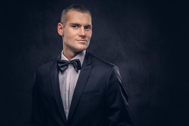 Close-up, a portrait of a handsome stylish man in an elegant black suit over a dark background.