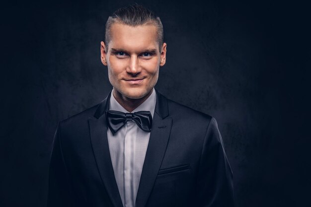 Close-up, a portrait of a handsome stylish smiling male in an elegant black suit over a dark background.