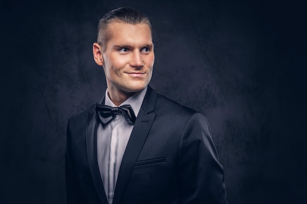 Close-up, a portrait of a handsome stylish smiling male in an elegant black suit over a dark background.