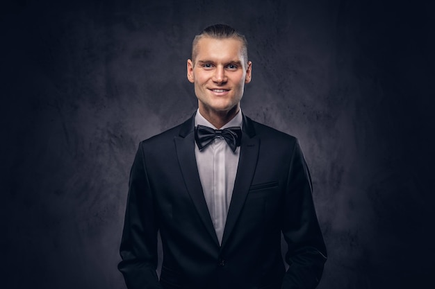 Close-up, a portrait of a handsome stylish smiling male in an elegant black suit over a dark background.