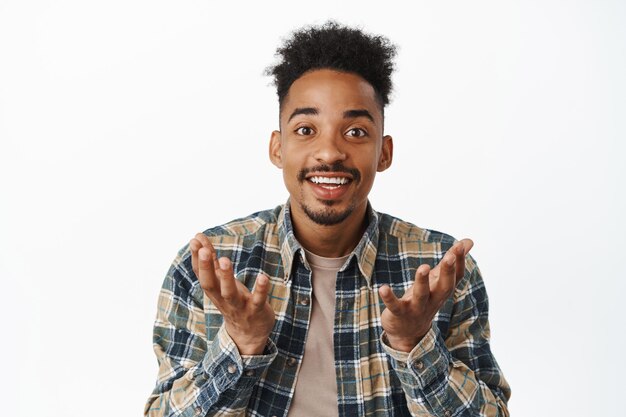 Close up portrait of happy african american man looking surprised and proud of you, raising hands as if holding smth in empty palms, making announcement, white background