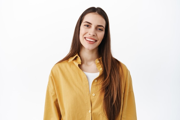 Free photo close up portrait of happy caucasian woman with long natural hair nude make up smiling and tilt head looking friendly and positive standing over white background