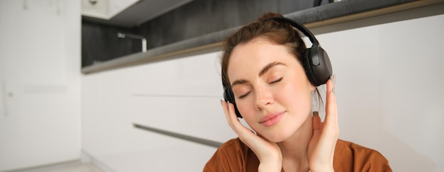 Free Photo close up portrait of happy smiling young woman listens to music in wireless headphones enjoys