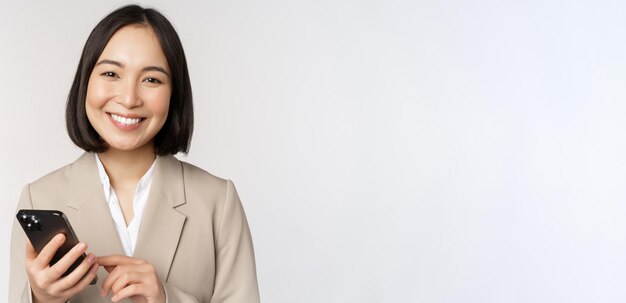 Close up portrait of korean woman corporate lady in suit using mobile phone and smiling holding smar