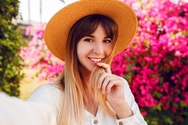 Close up portrait of lovely girl in trendy straw hat making selfie portrait