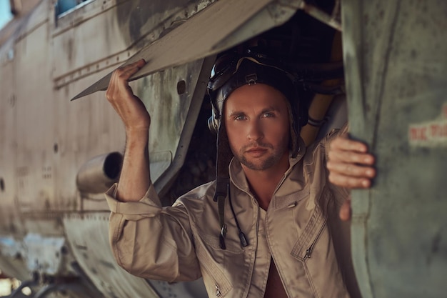 Close-up portrait of a mechanic in uniform and flying near, standing under an old bomber airplane in the open air museum.