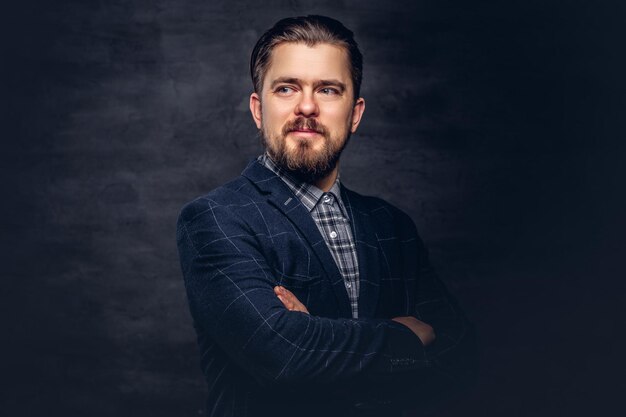 Close-up portrait of a middle-aged man with beard and hairstyle dressed in an elegant blue suit on a textured dark background in studio.