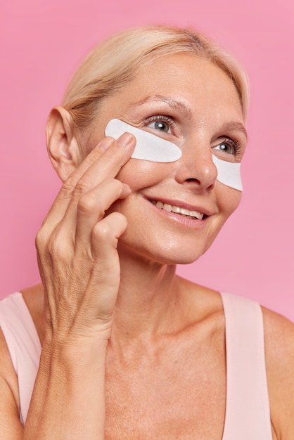 Close up portrait of middle aged woman applies beauty patches under eyes