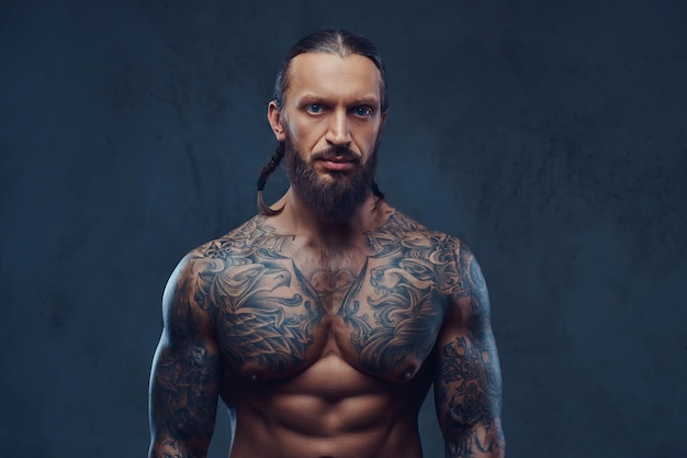 Free photo close-up portrait of a muscular bearded tattoed male with a stylish haircut. isolated on a dark background.