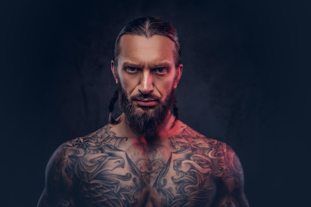 Close-up portrait of a muscular bearded tattoed male with a stylish haircut. Isolated on a dark background.