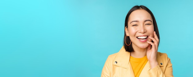 Close up portrait of natural asian girl laughing smiling and looking happy standing over blue background