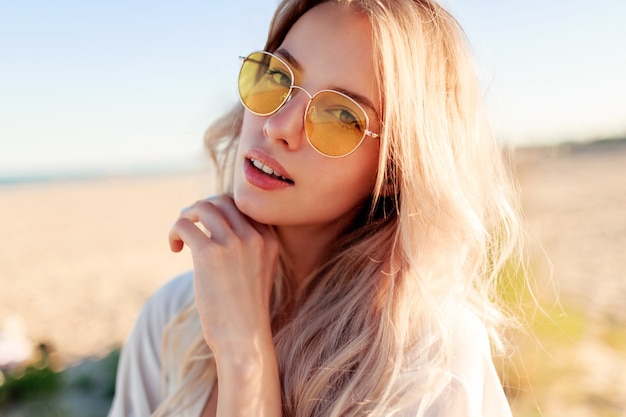 Close up portrait of playful smiling  blonde girl playing with hairs, having fun and enjoying summer on the beach .