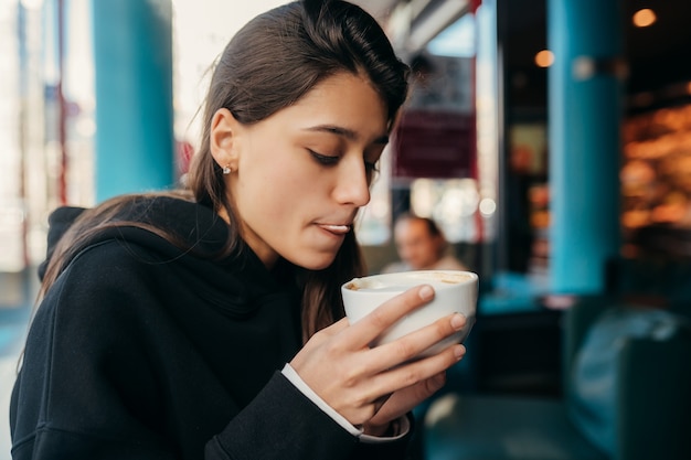 Close up portrait of pretty female drinking coffee. Lady holding a white mug with hand.