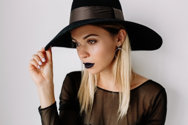 Close up portrait of pretty lovable woman with blond hair wearing hat posing over isolated wall