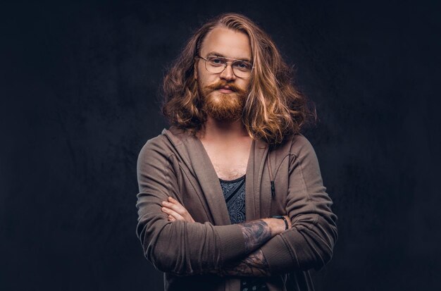 Free photo close-up portrait of a redhead hipster male with long luxuriant hair and full beard dressed in casual clothes standing in a studio, looking away. isolated on a dark background.