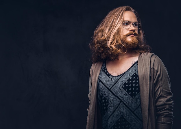 Free Photo close-up portrait of a redhead hipster male with long luxuriant hair and full beard dressed in casual clothes standing in a studio, looking away. isolated on a dark background.