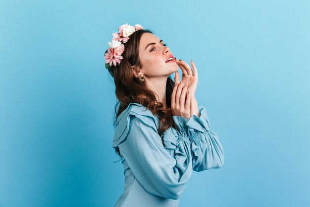 Close-up portrait of sensual girl in silk blouse with frill. Lady with flowers in hair touching lips.