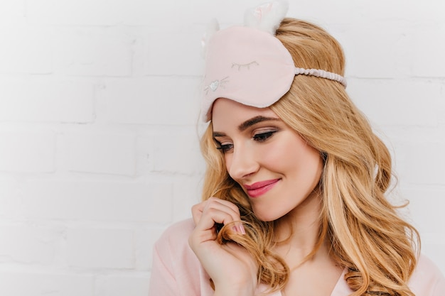 Free Photo close-up portrait of shy caucasian woman enjoying morning. carefree european girl in eyemask standing on white wall.