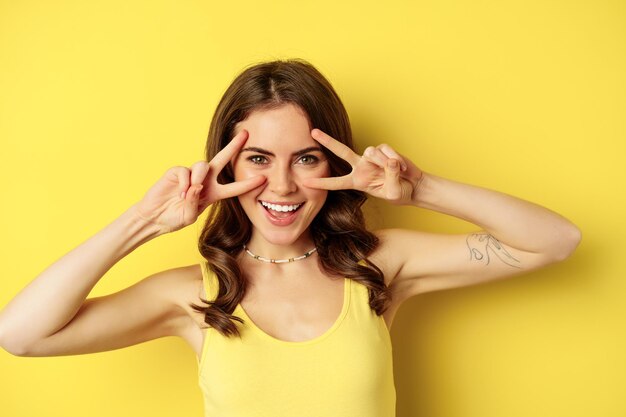 Close up portrait of smiling beautiful girl showing peace vsign and looking happy posing for summer ...