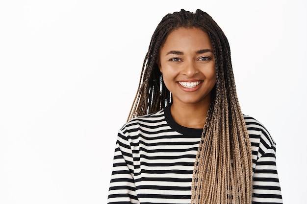 Free photo close up portrait of smiling black girl looking relaxed and happy standing in striped blouse against white background