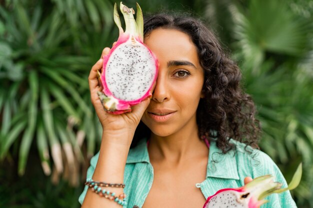 Close up portrait of smiling lovely brunette woman  with wavy hairs holding  tropical fruits