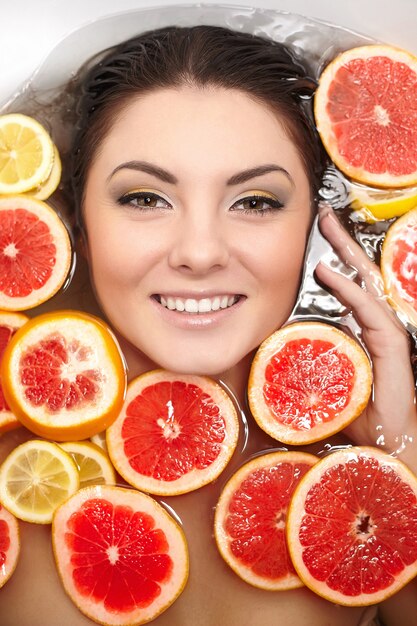 Close up portrait of smiling woman with many juicy citrus fruit lemon grapefruit in bathroom