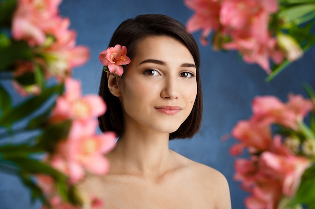 Close up portrait of tender  young woman with blured pink flowers over blue wall